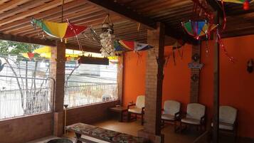 A room with a wooden ceiling, a bench, and several chairs. There are colorful decorations hanging from the ceiling.