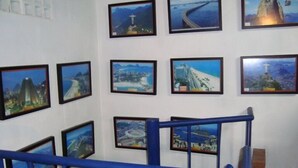 A staircase with blue railings leading to a landing where framed pictures of various landmarks are displayed on the wall. - Albergue Piratas do Sol - Hostel (Recife)