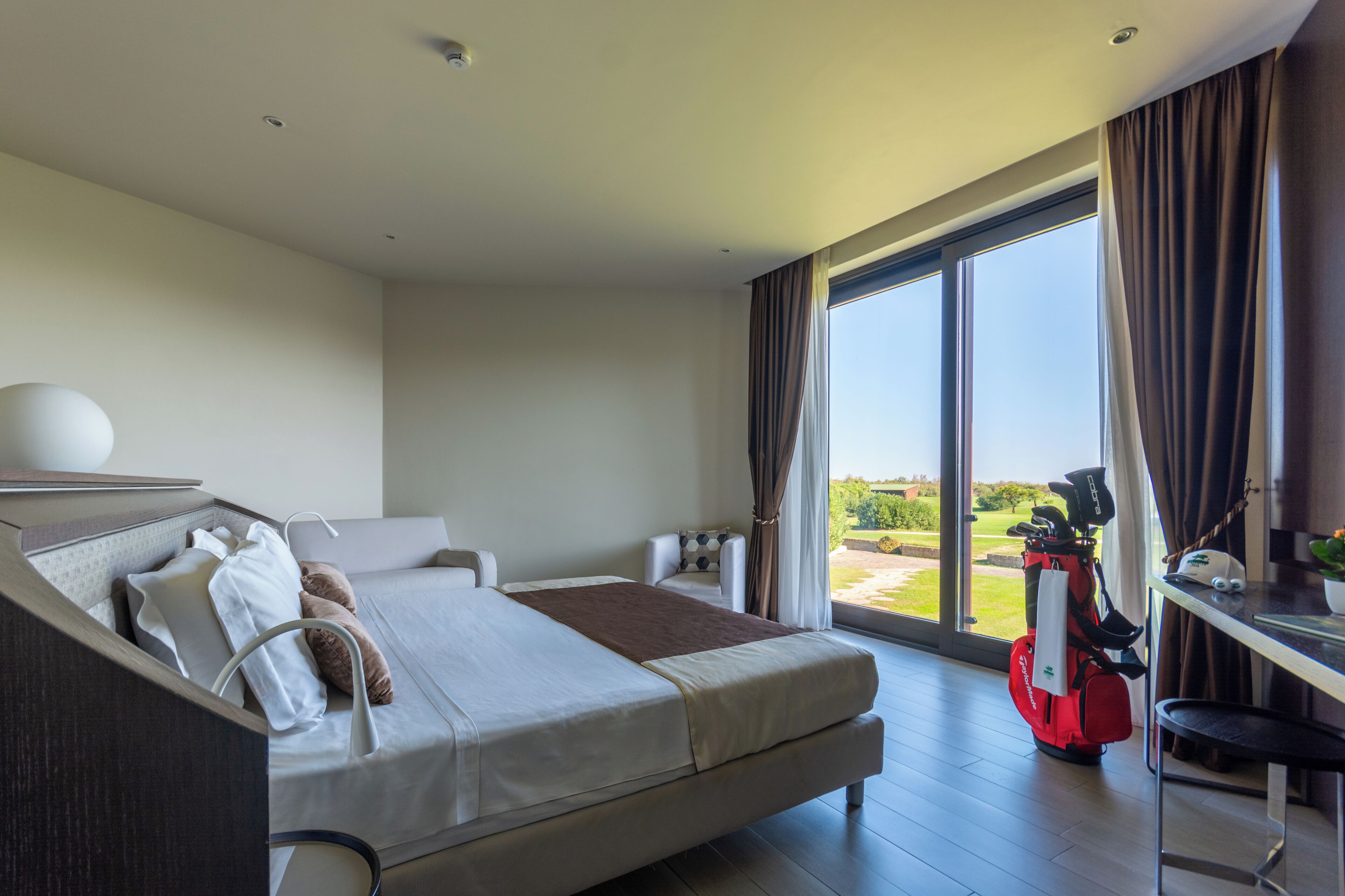 A modern hotel room with a large bed, a desk, and a view of the outdoors.