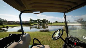 Polsterung im Innenraum eines Golfcarts, mit Lenkrad und Armaturenbrett, Blick auf einen Teich und einen Golfplatz.