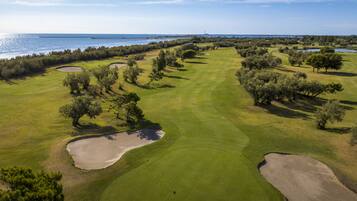 Vista aerea di un campo da golf con bunker di sabbia, alberi e uno specchio d'acqua sullo sfondo.