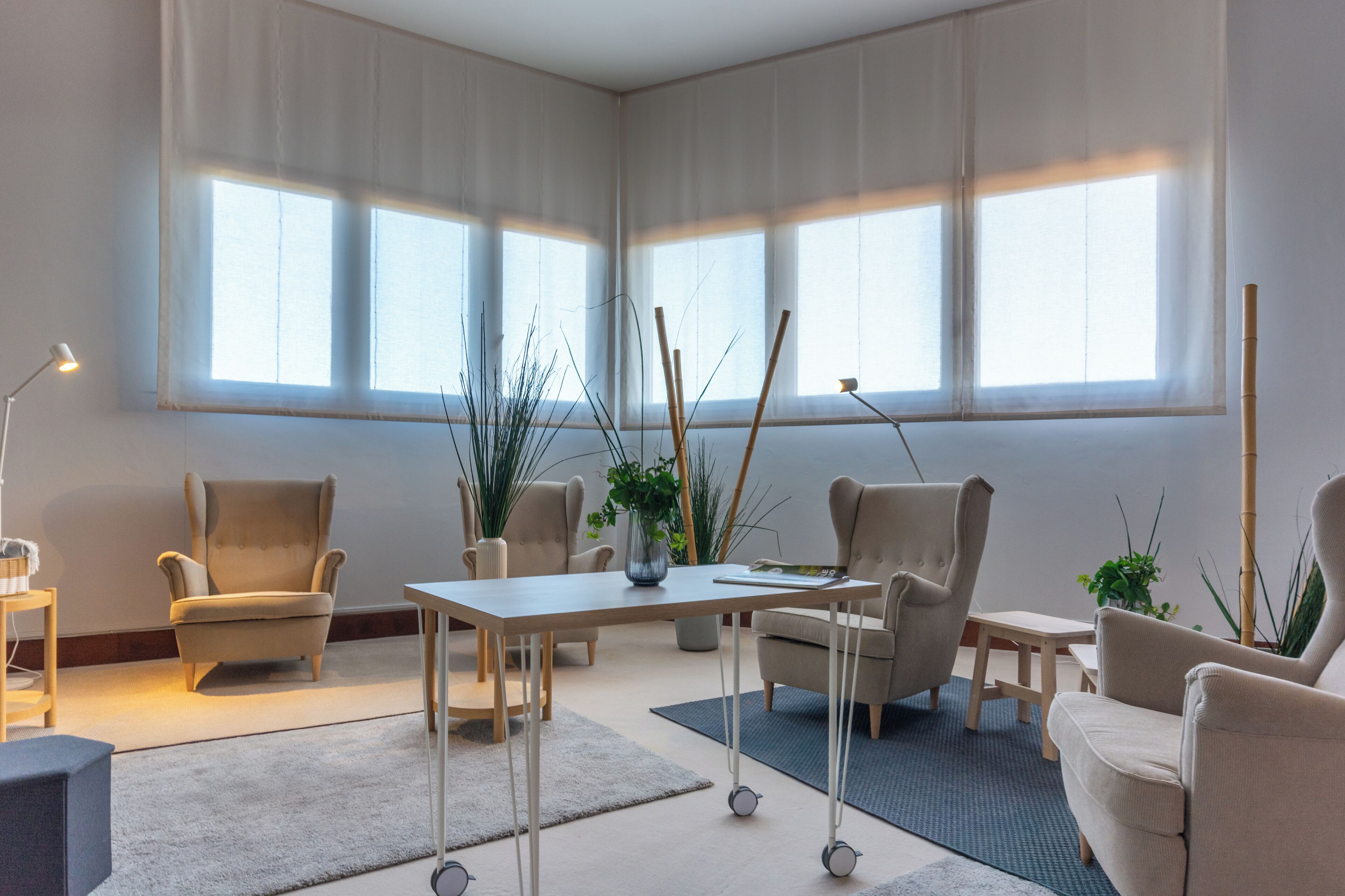 Een ruime kamer met een groot raam, een tafel, stoelen en potplanten.