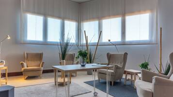 Een ruime kamer met een groot raam, een tafel, stoelen en potplanten.