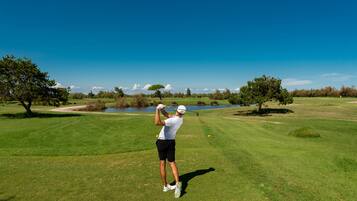 A golf course with a clear sky, a golfer in mid-swing, and a pond in the background.