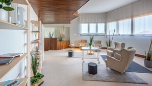 A modern living room with a wooden ceiling, a bookshelf, a coffee table, and two armchairs. - Isola di Albarella Golf Hotel (Rosolina)