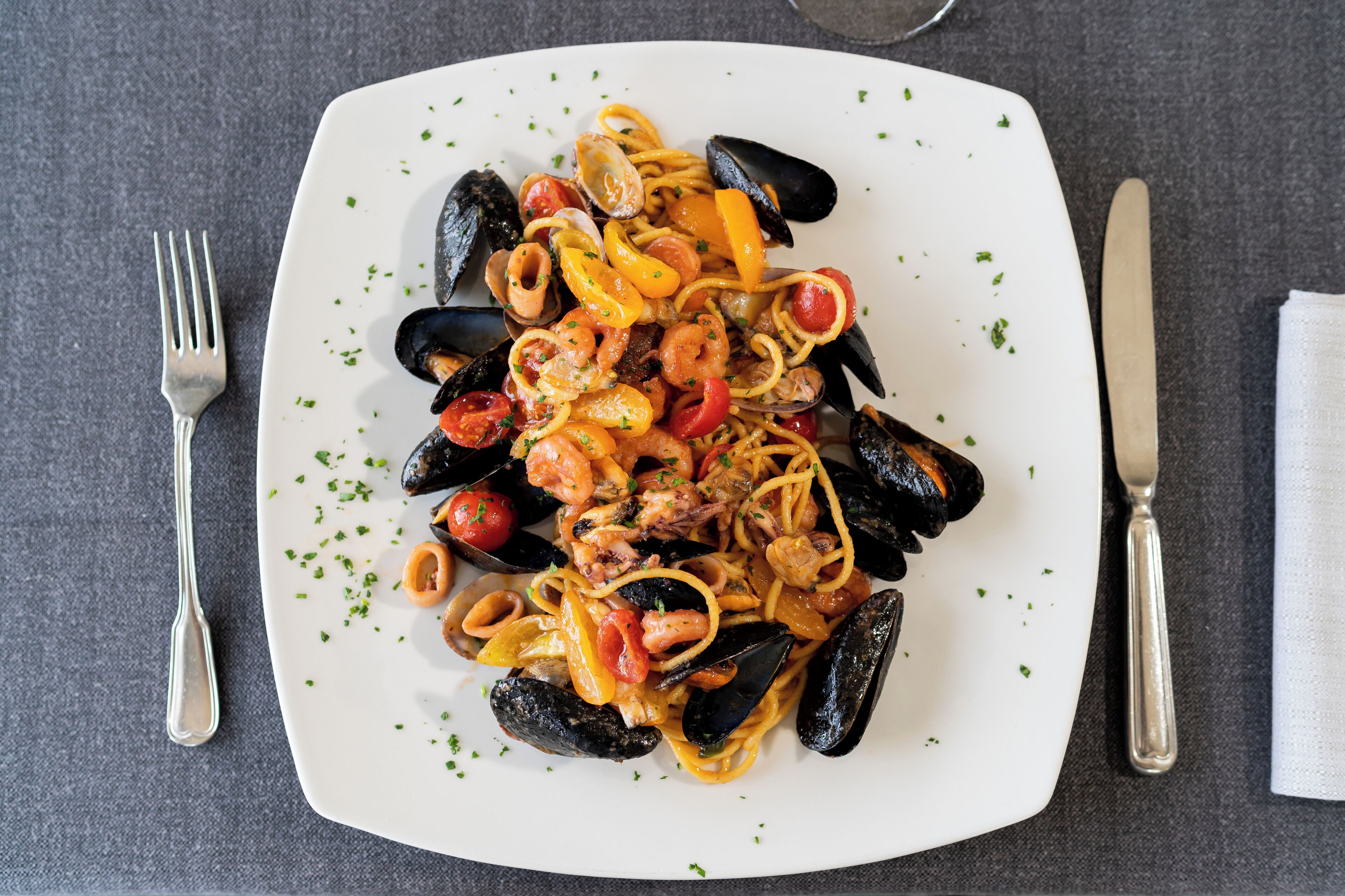 A plate of seafood pasta with mussels, shrimp, and tomatoes, garnished with herbs.