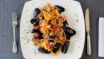 A plate of seafood pasta with mussels, shrimp, and tomatoes, garnished with herbs.