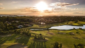 A golf course with bunkers, water hazards, and a sunset in the background. - Isola di Albarella Golf Hotel (Rosolina)