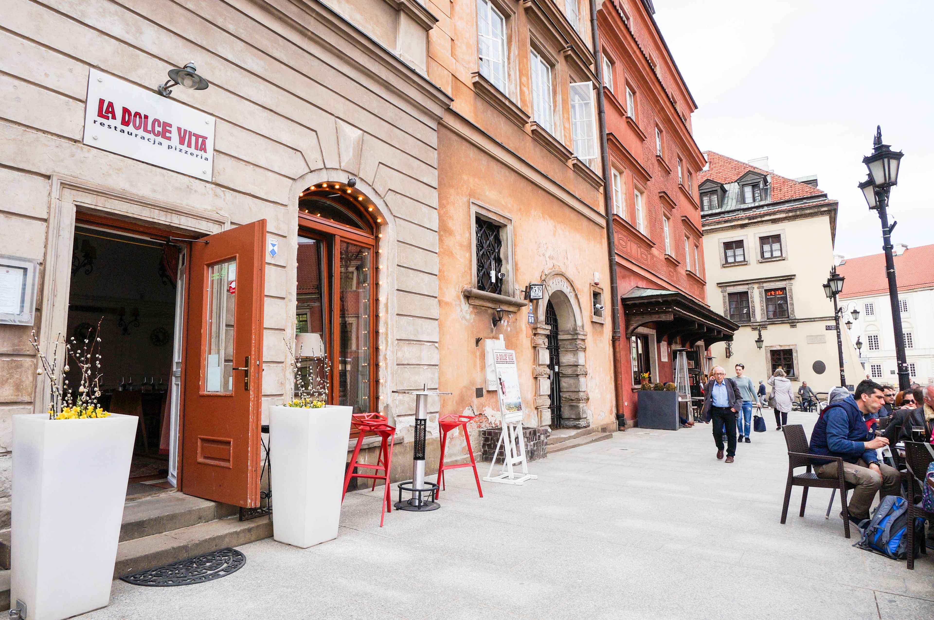 A building with a sign reading "LA DOLCE VITA" and outdoor seating with tables and chairs.