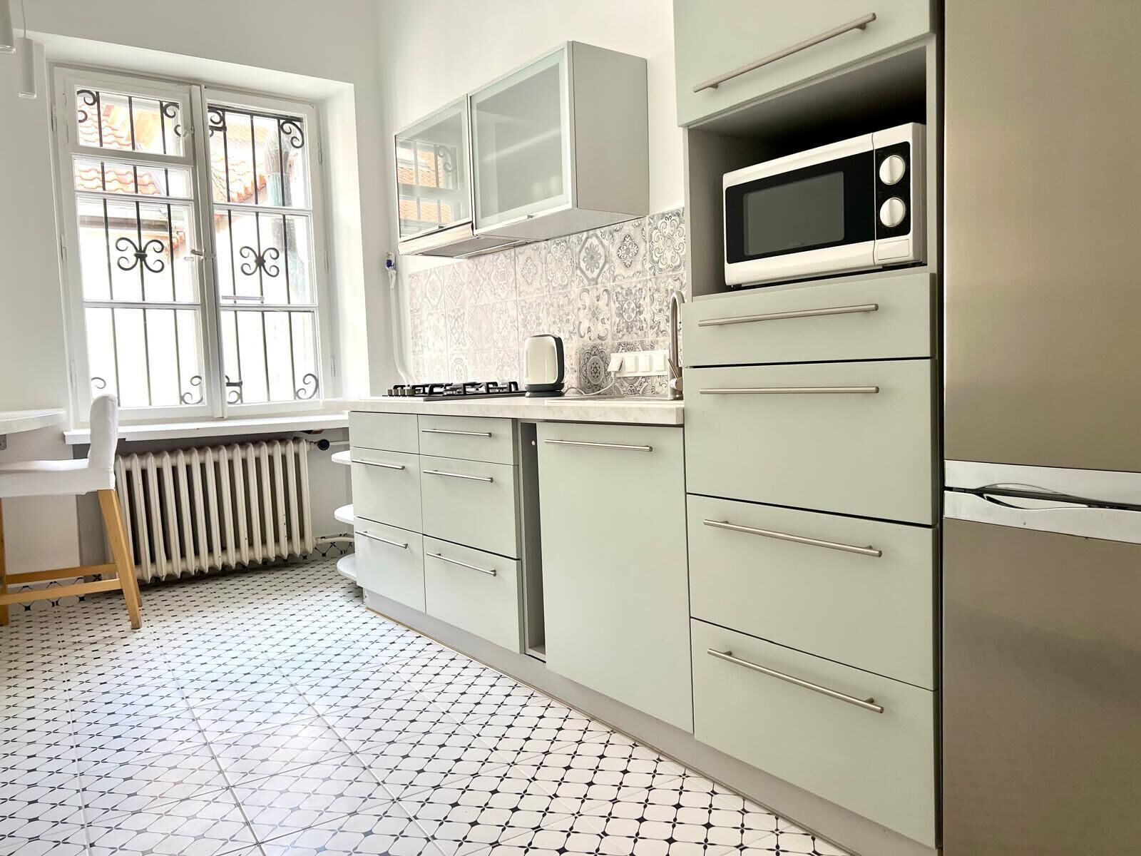 A kitchen with white cabinets, a microwave, and a window with decorative bars.
