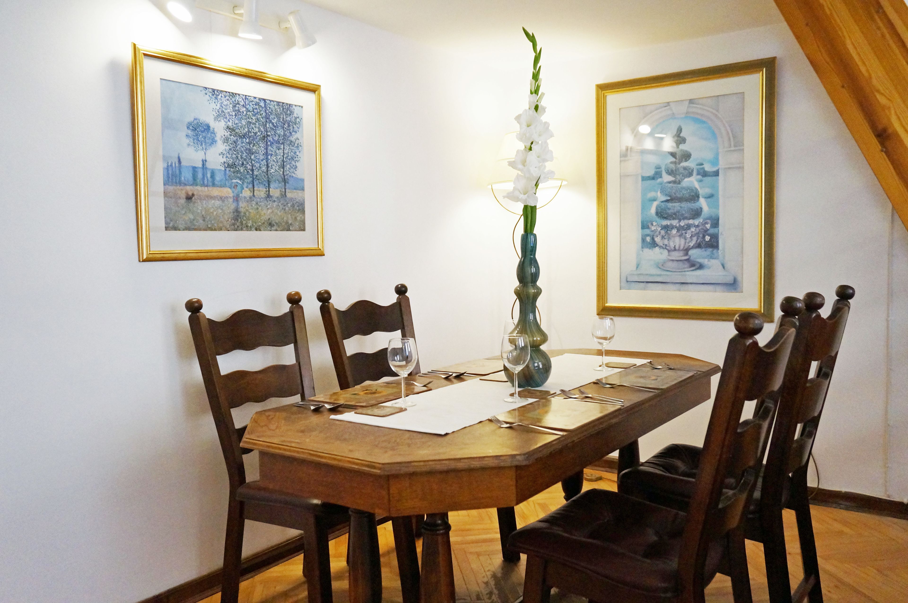 Una mesa de comedor con sillas, obras de arte enmarcadas en las paredes y un jarrón con flores.