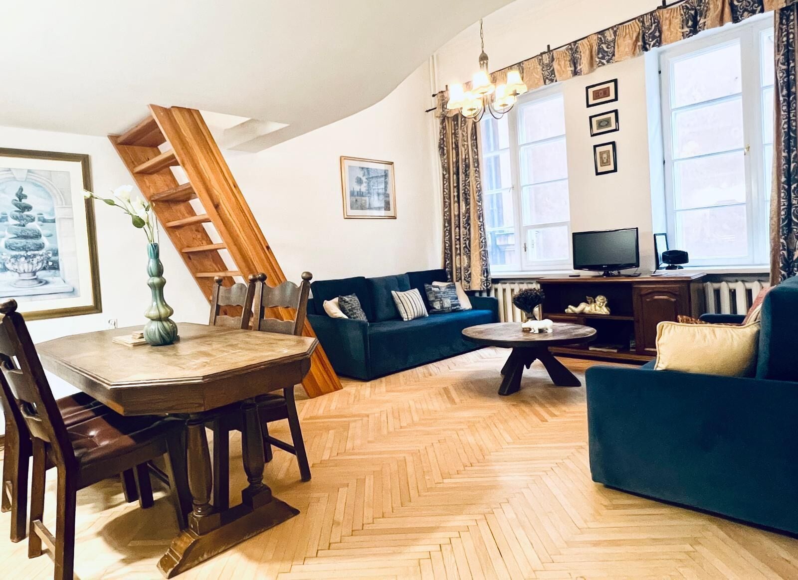 A living room with a herringbone floor, a blue sofa, a wooden coffee table, and a television.