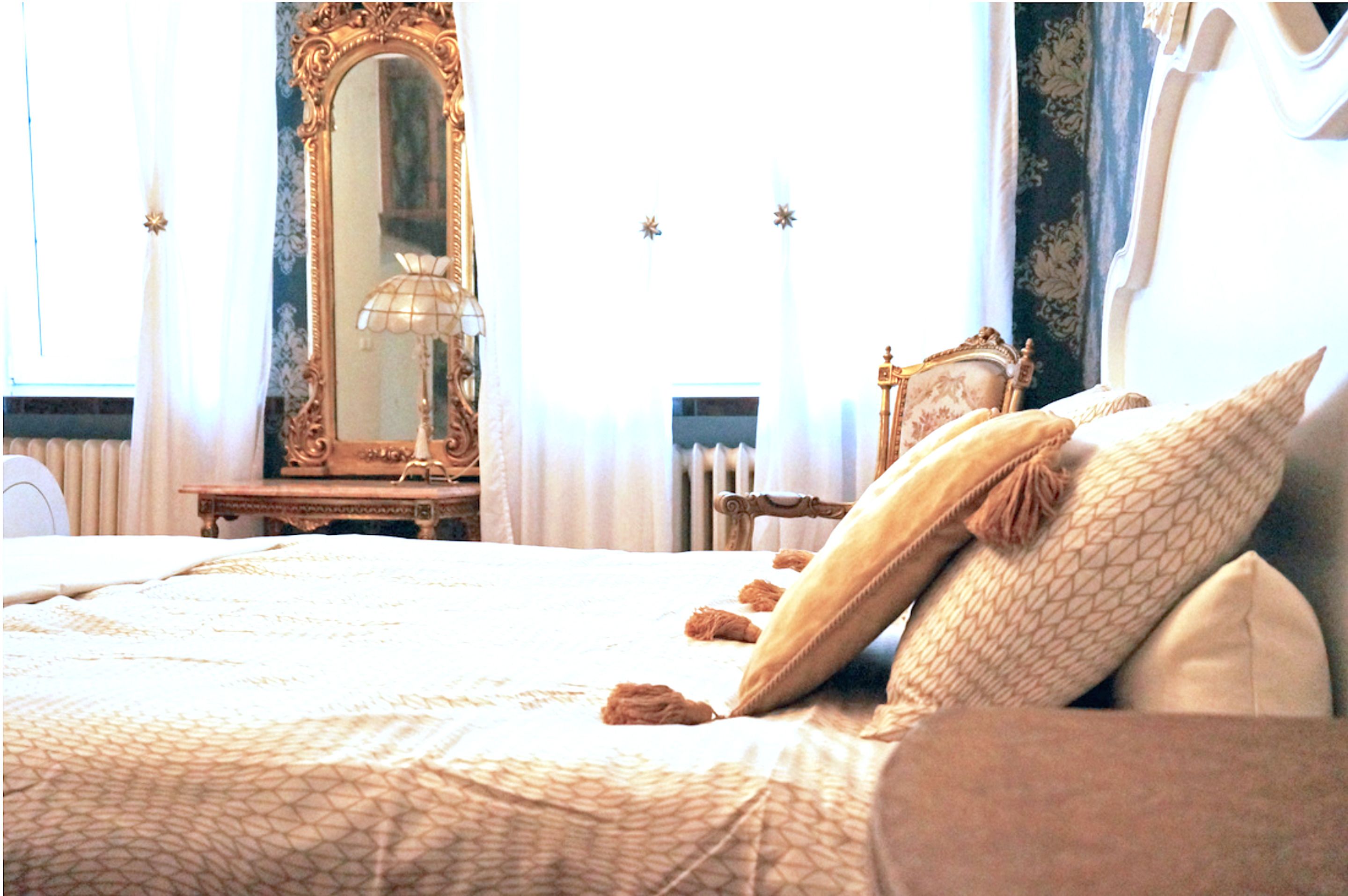 A bedroom with a large bed, a dresser, a mirror, and a window with curtains.
