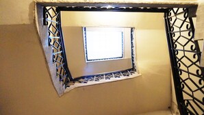 Una pequeña ventana con marco de metal y detalles decorativos, ubicada en un rincón de una habitación con paredes lisas.