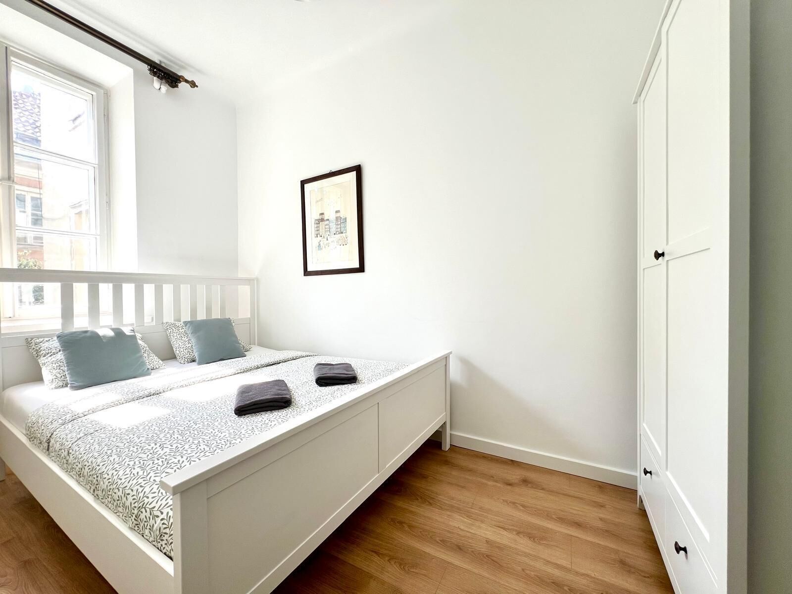 Un dormitorio con una cama, un armario blanco y un cuadro en la pared.