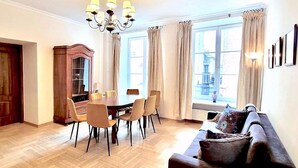 A dining area with a wooden table and chairs, a chandelier, and large windows with curtains. - AAA STAY Castle Square Old Town (Warsaw)