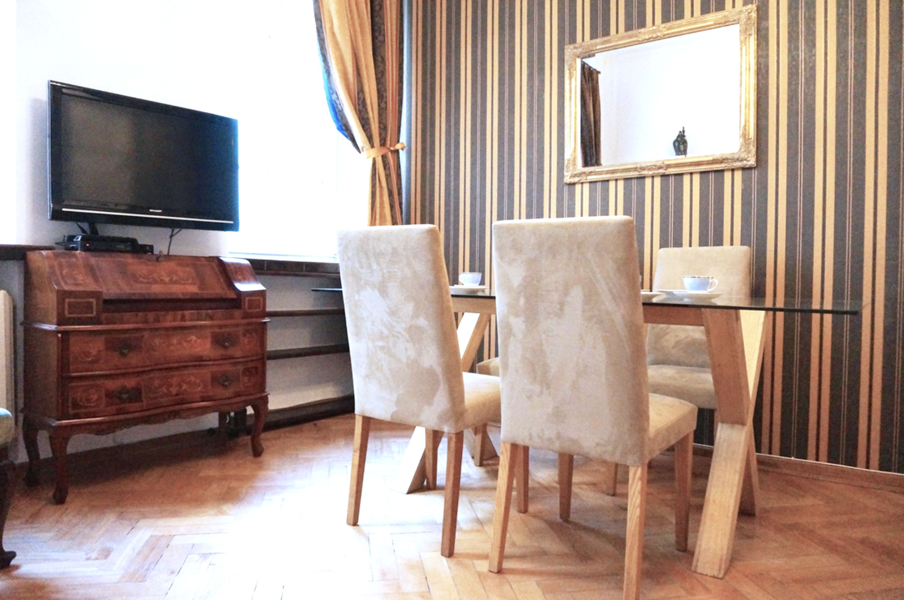 Een kamer met een houten dressoir, een televisie, een eettafel met stoelen en een spiegel aan de muur.