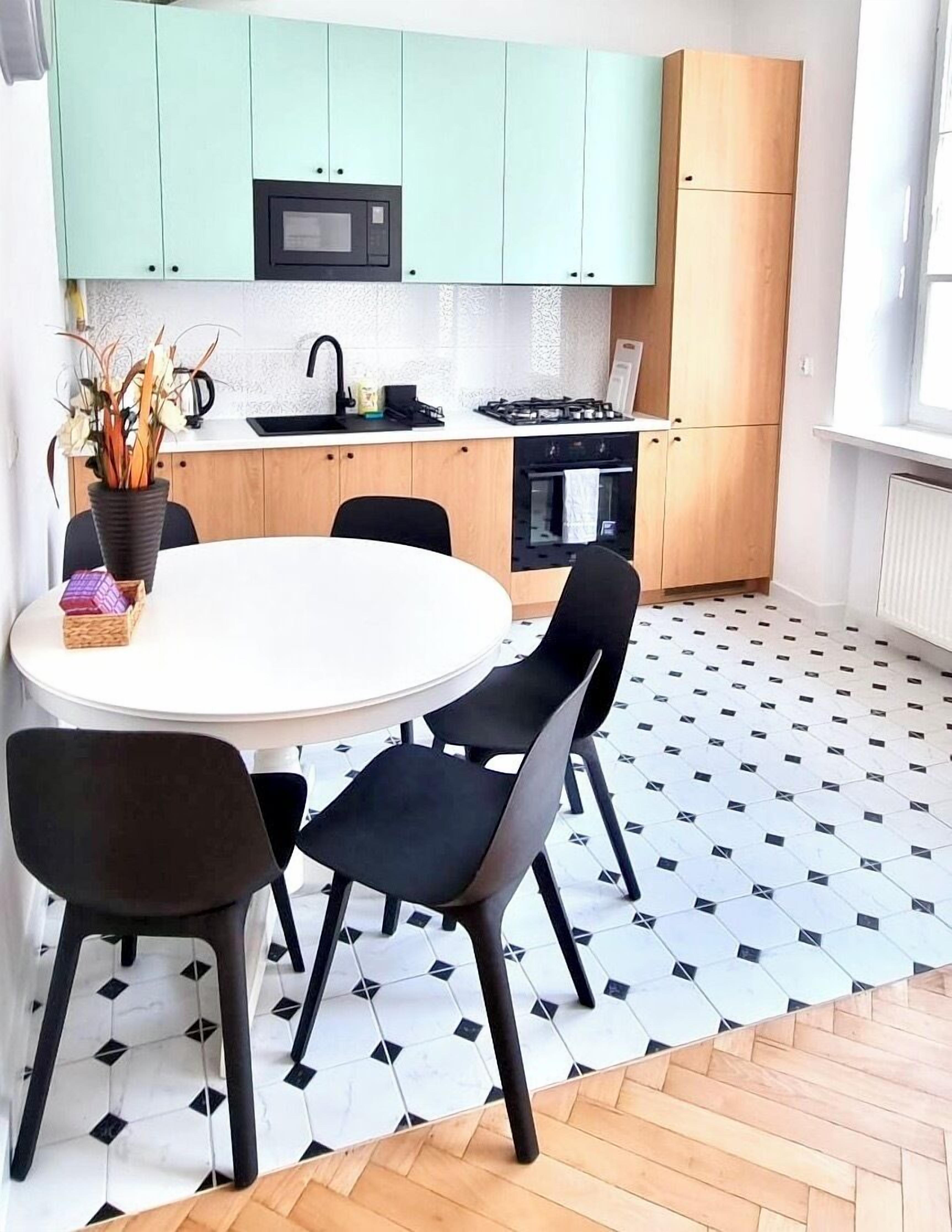 A modern kitchen with teal cabinets, a white dining table, and black chairs.
