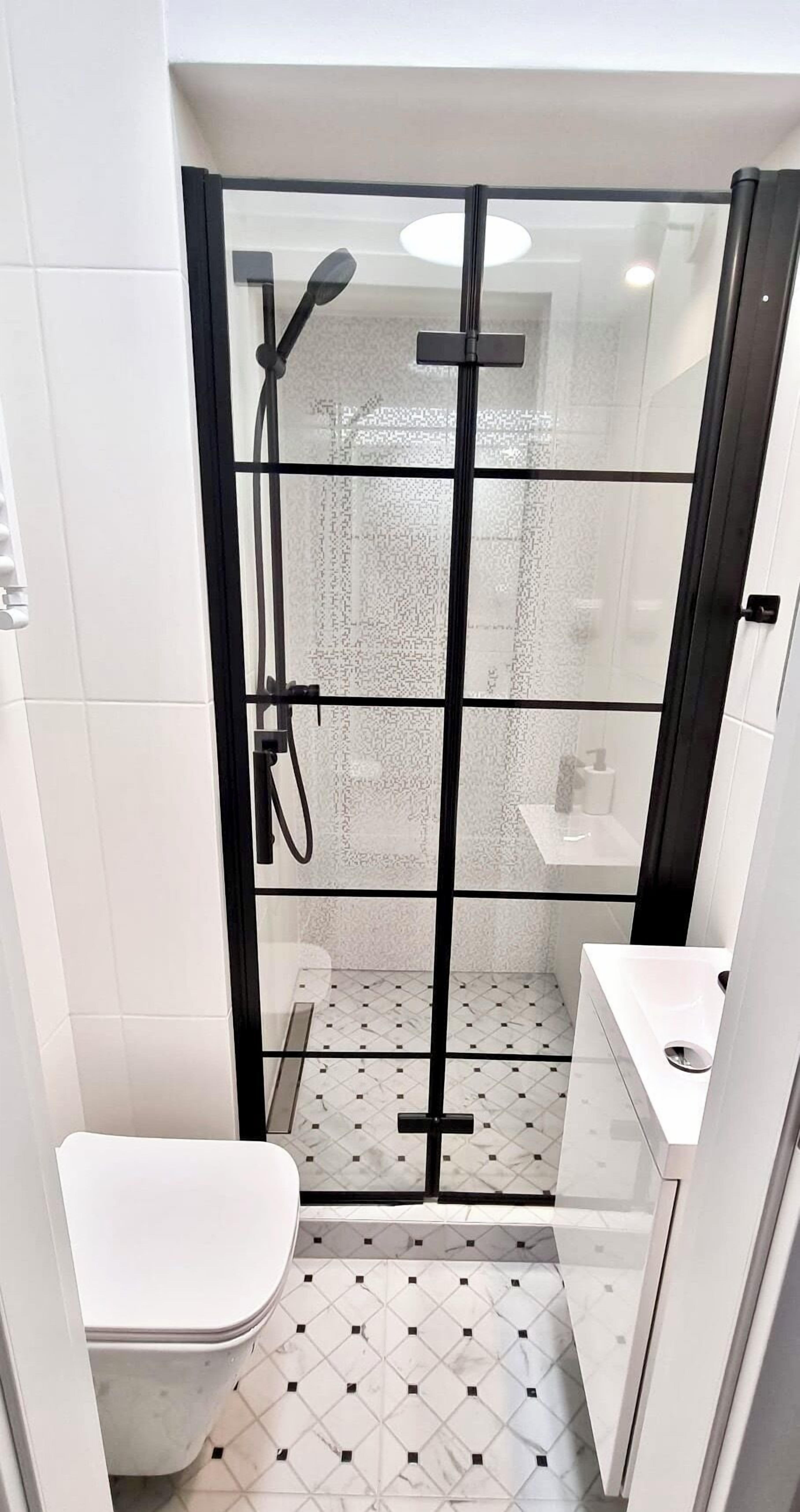 Un baño pequeño con ducha envuelta en vidrio, azulejos blancos y un inodoro blanco.