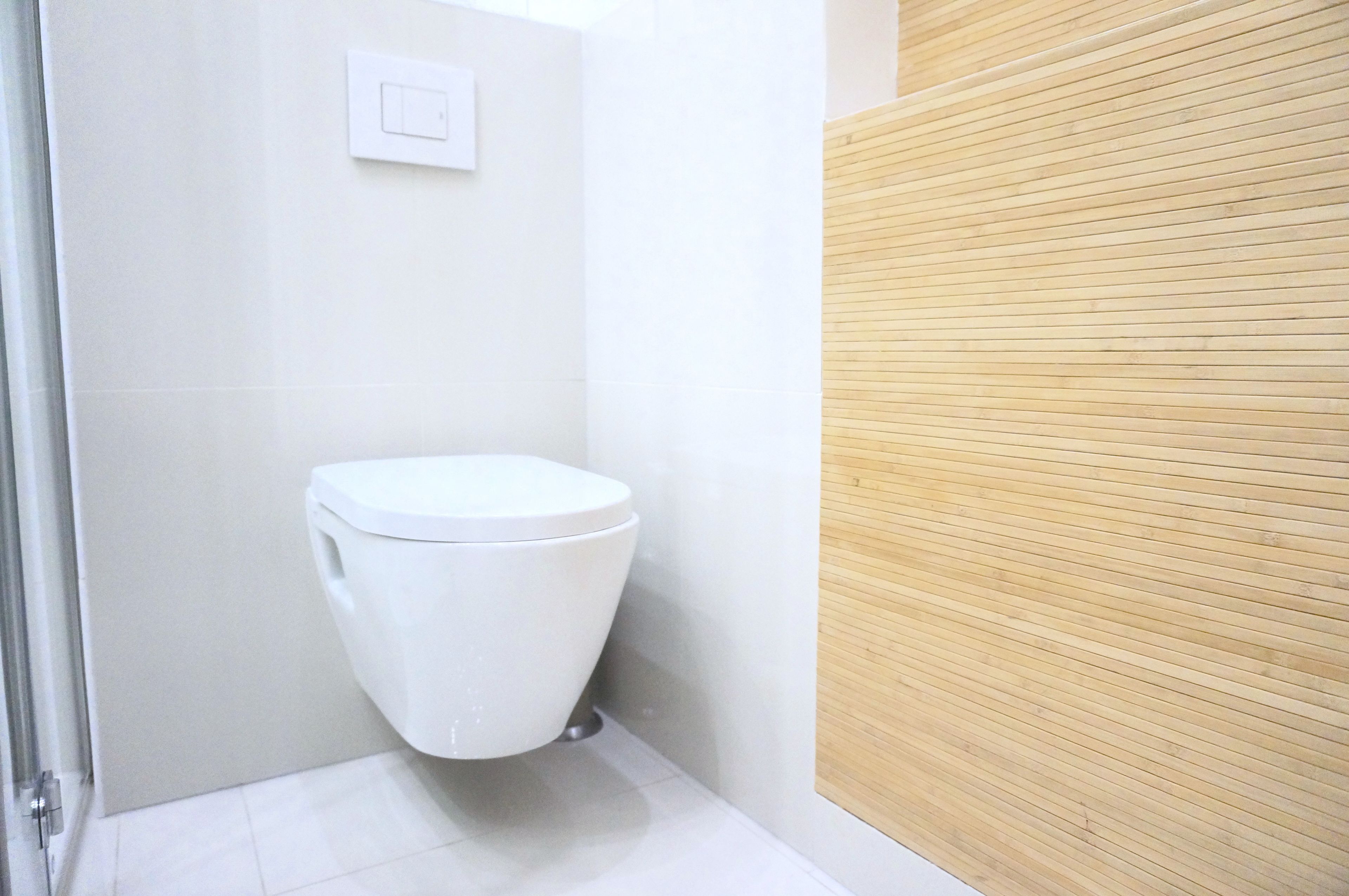 A modern bathroom with a white toilet, a wooden panel wall, and a tiled floor.