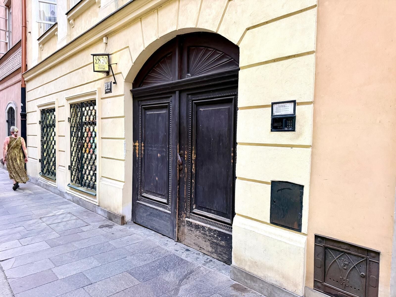 A building with double doors, a sign above the door, and a small plaque on the wall.