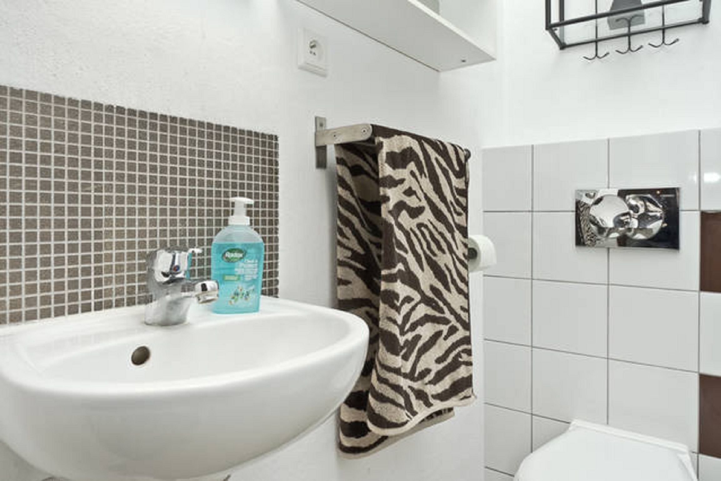 A bathroom with a white sink, zebra-patterned towel, and a small mirror with a decorative item.