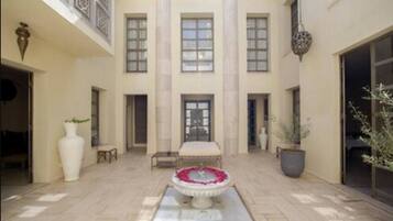 A spacious courtyard with a central fountain, a seating area, and a large windowed entrance.