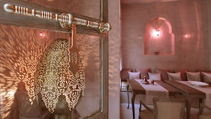 A dining area with a long table, chairs, and a patterned wall hanging. - Riad Joya (Marrakech)