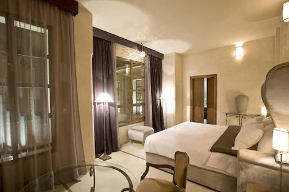 A hotel room with a bed, a chair, a desk, and a lamp.