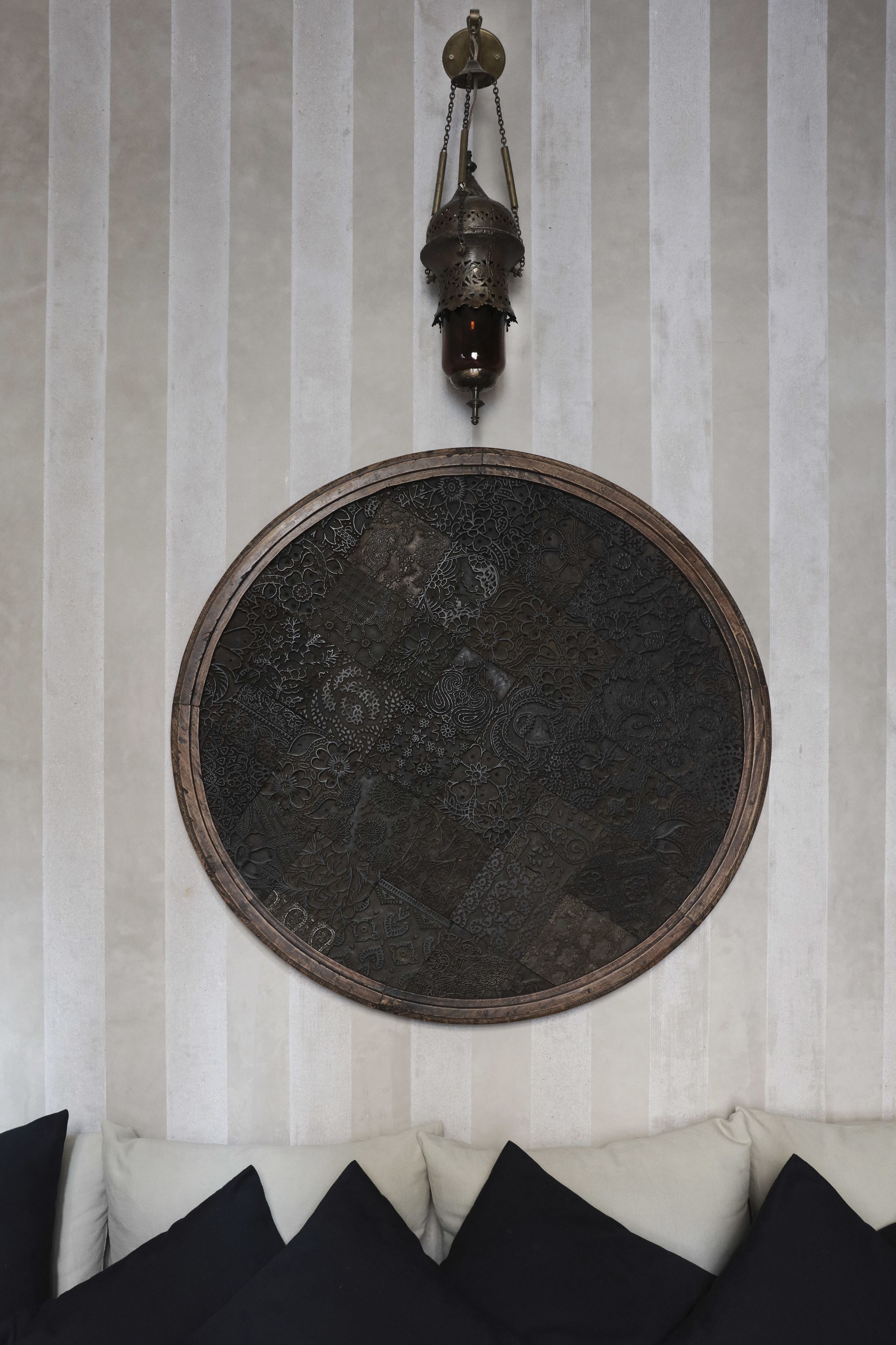 A room with a striped wall, a round decorative plate, and a hanging lantern.