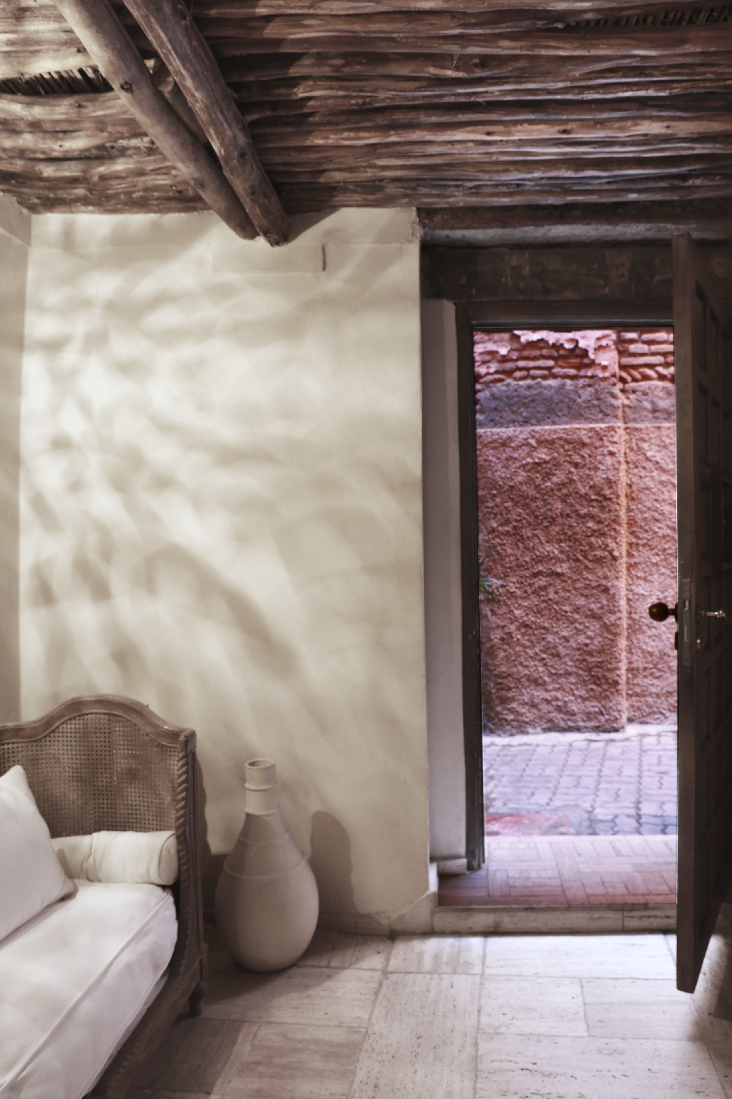 A room with a wicker sofa, a large vase, and a wooden ceiling.