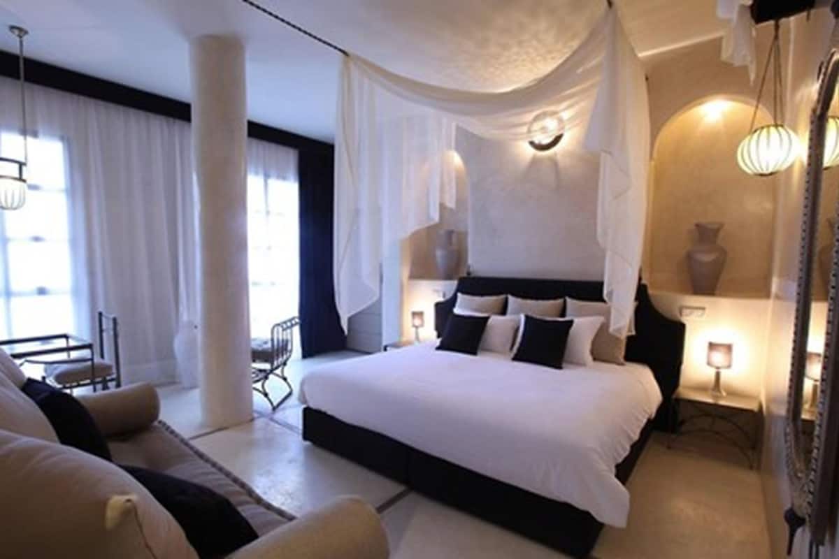 A bedroom with a large bed, a chair, a bedside table, and a window with curtains.