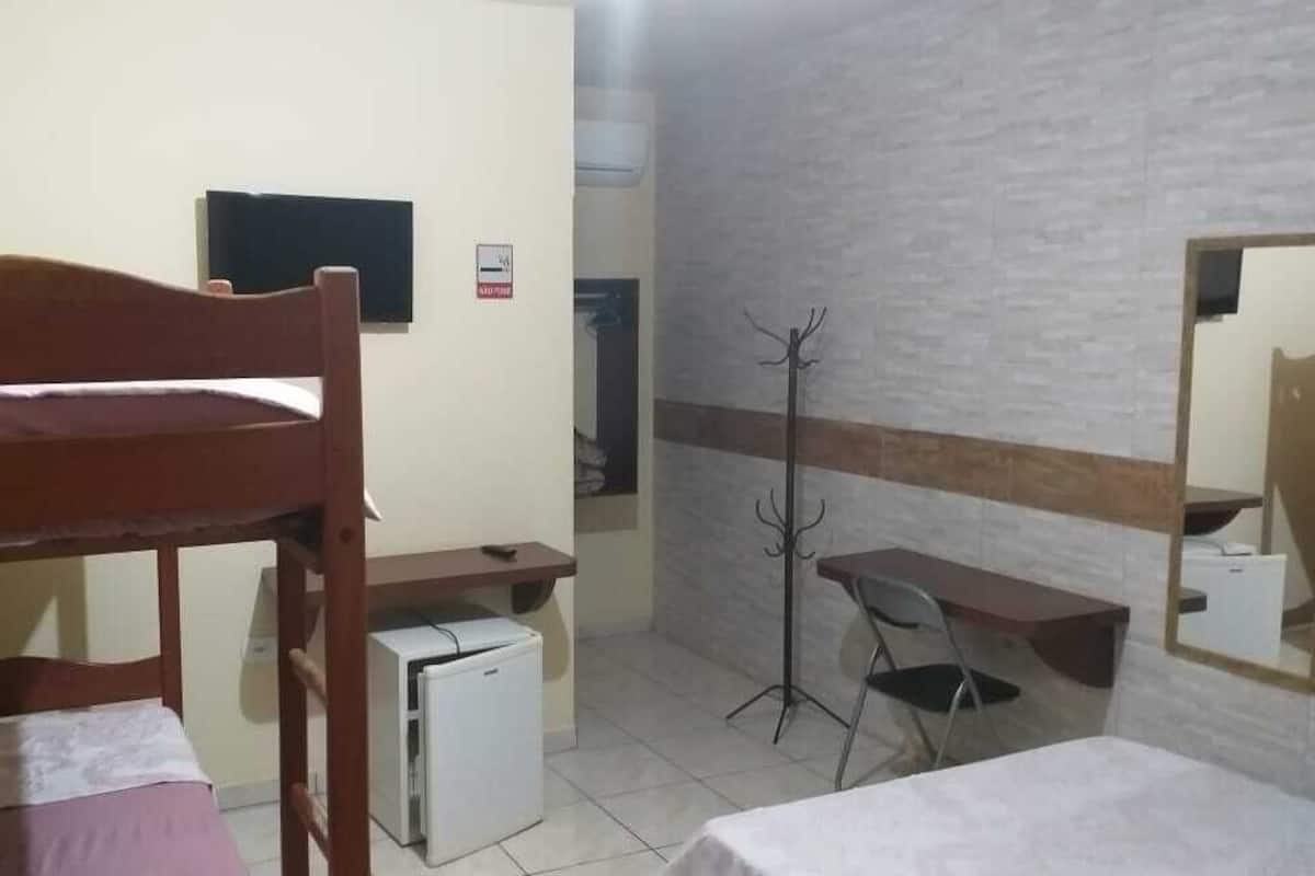 A dormitory room with bunk beds, a desk, a chair, a coat rack, and a small refrigerator.