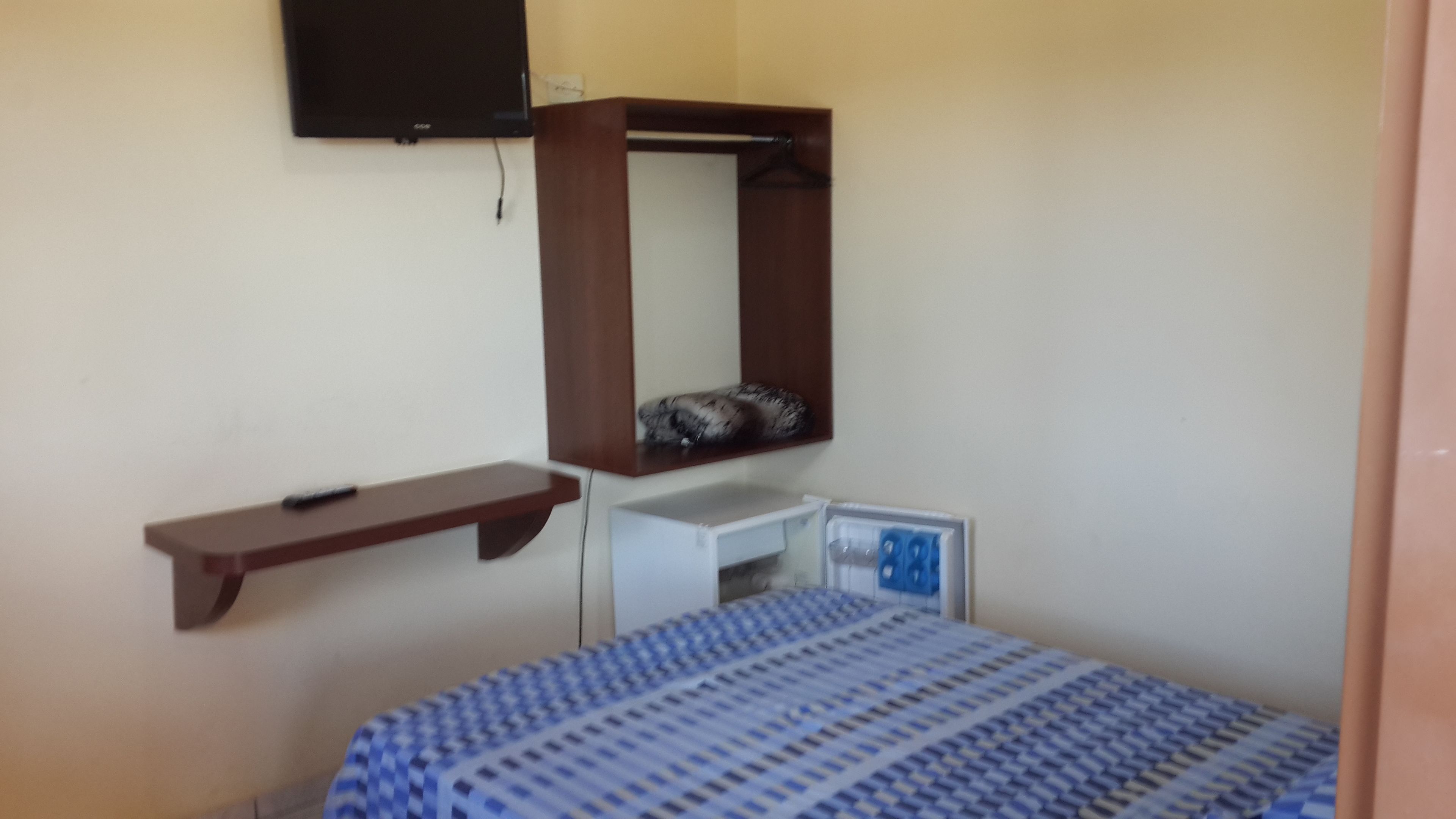A bedroom with a bed, a small desk, a mirror, and a TV mounted on the wall.