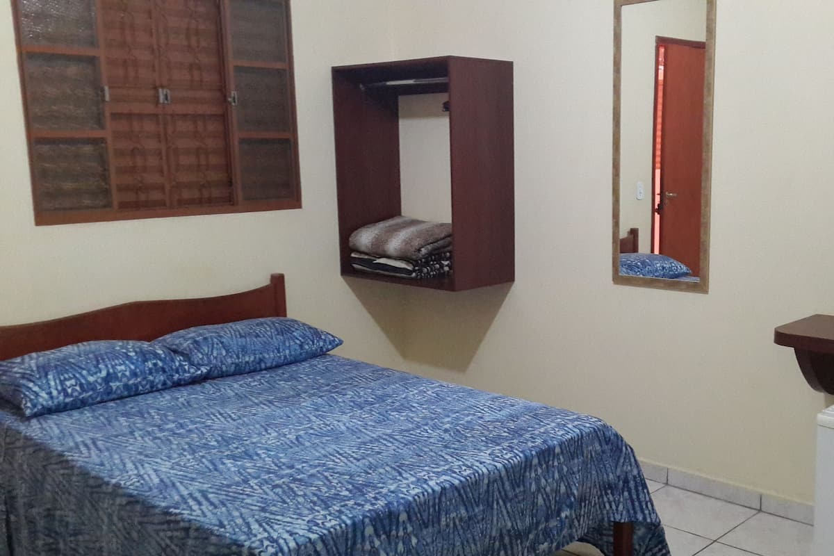 A bedroom with a bed, a wardrobe, a mirror, and a small white appliance.