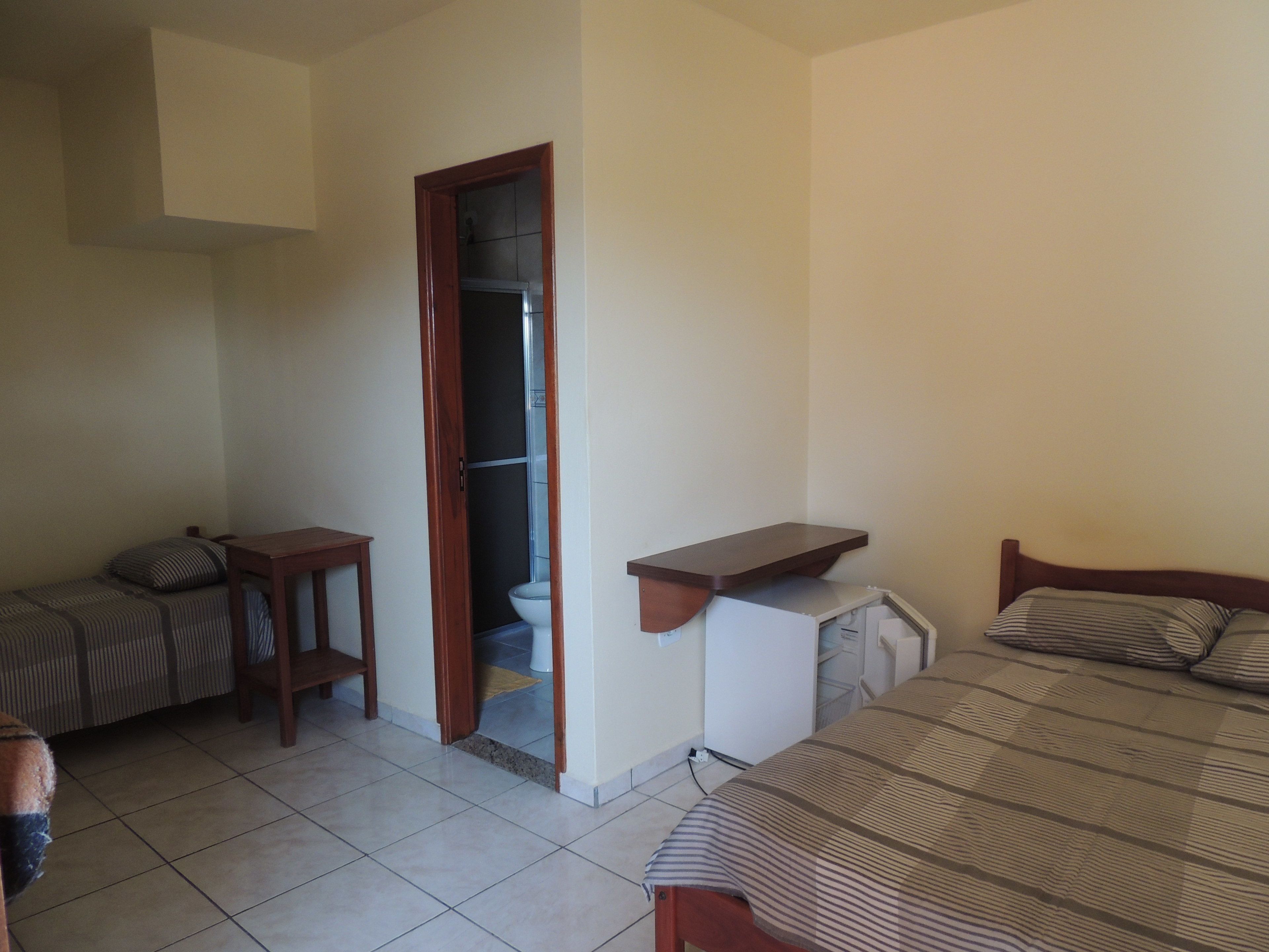 A room with a bed, a small table, a desk, and a bathroom door.