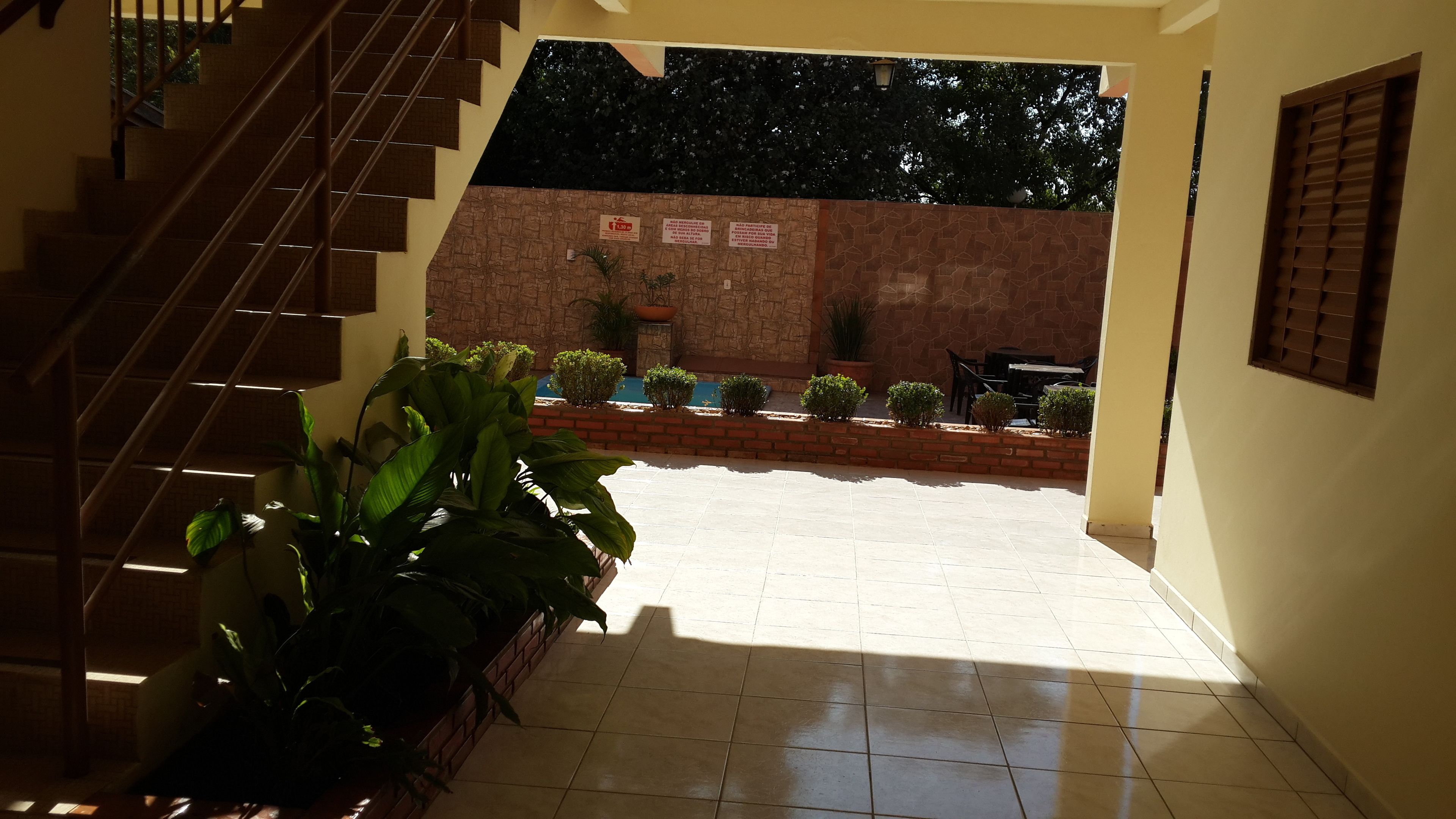 A staircase leading to a covered outdoor area with tiled flooring, potted plants, and a brick wall.