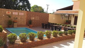 A swimming pool surrounded by a brick wall, with potted plants and outdoor furniture. - Pousada Paraiso (Bonito)