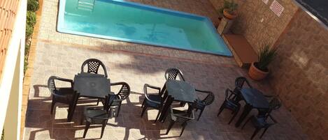 Piscina con escalera, rodeada de un patio con suelo de piedra y mobiliario exterior.