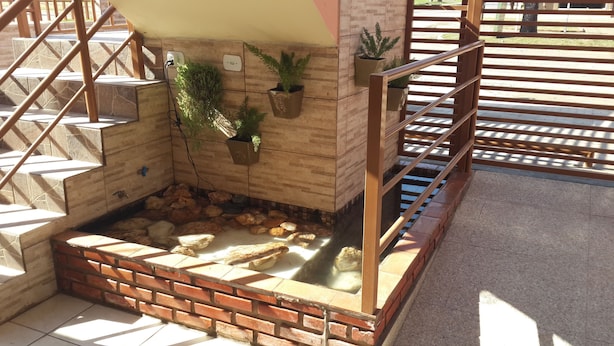 A staircase with a brick base, wooden steps, and a metal railing. There are potted plants on the wall and a small water feature at the bottom. - Pousada Paraiso (Bonito)