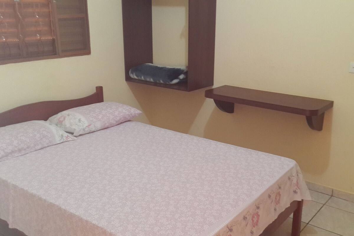A bedroom with a bed, a bedside table, a mirror, and a shelf.