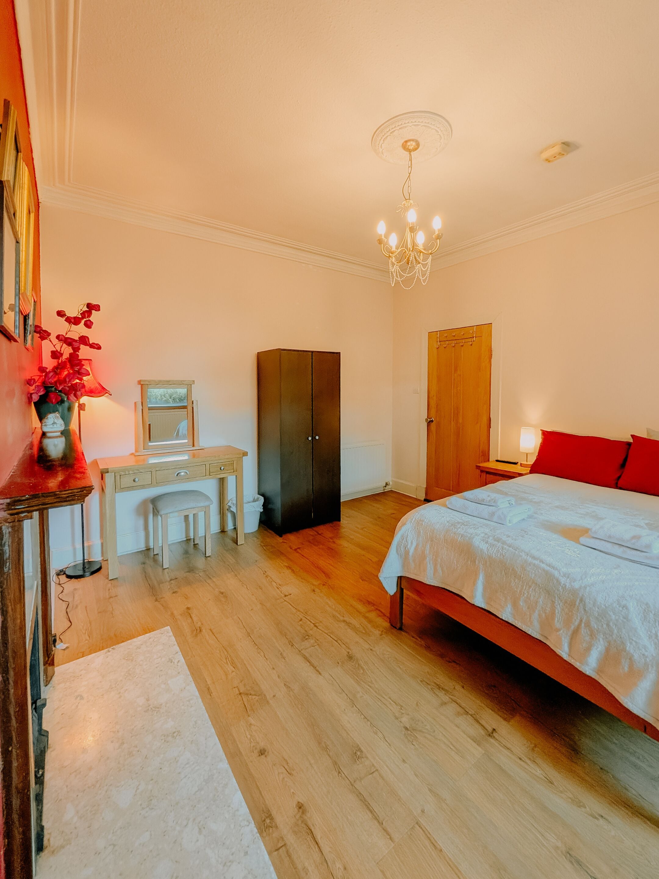 A bedroom with a bed, a desk, a chair, a wardrobe, and a chandelier.