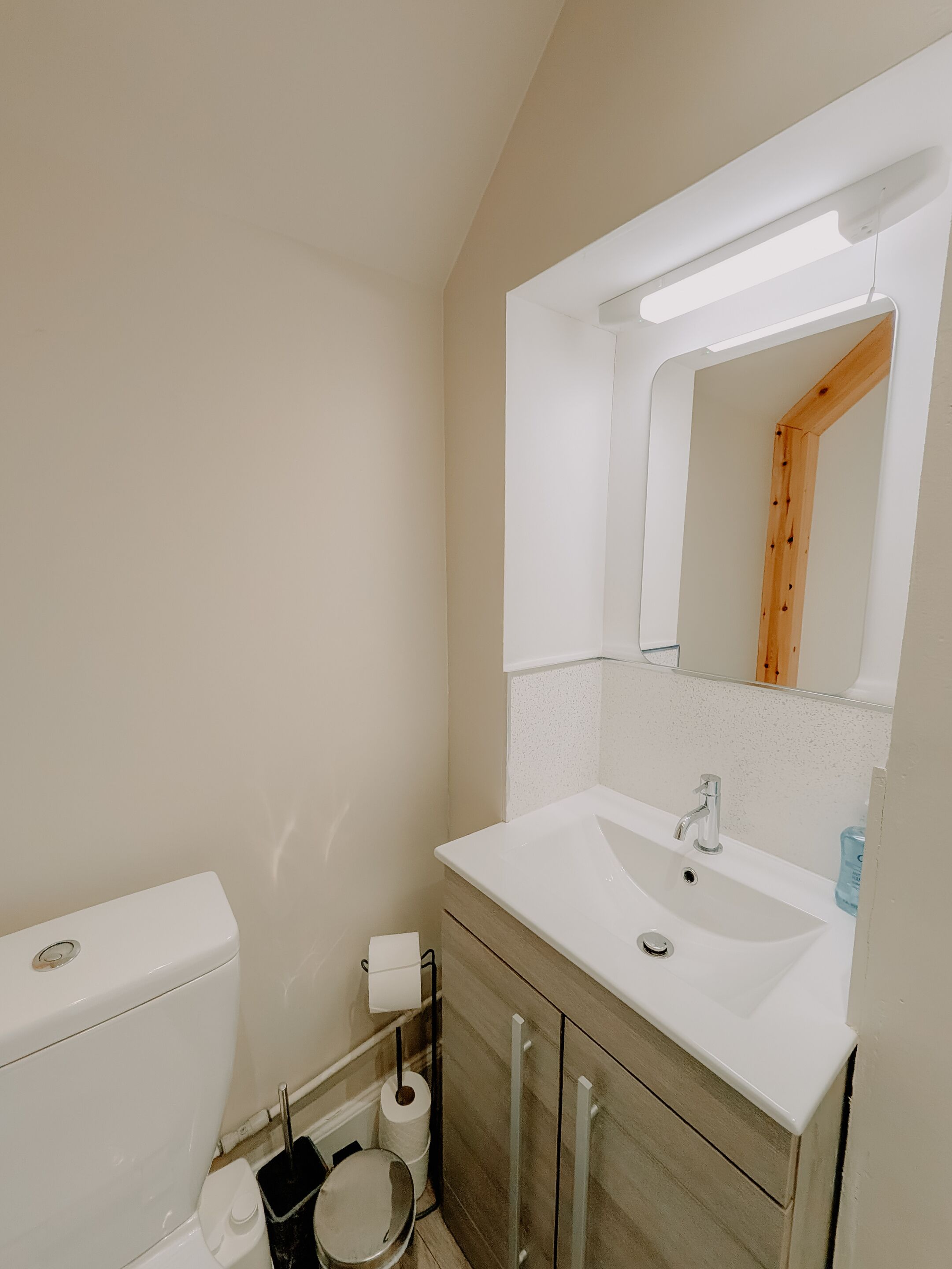 A bathroom with a toilet, sink, mirror, and a towel rack.