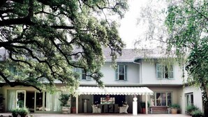 A two-story house with a covered patio area, a lawn, and a large tree in the foreground. - Hoeveld House (Sandton)