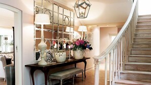 A wooden staircase with a white railing, a bench, and a table with decorative items and flowers. - Hoeveld House (Sandton)