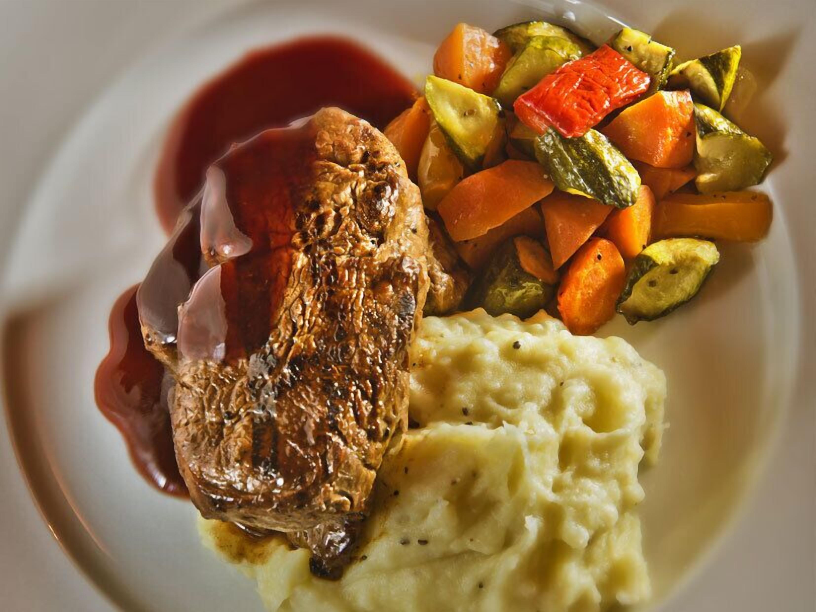 Un plato con filete, puré de papas y verduras asadas.