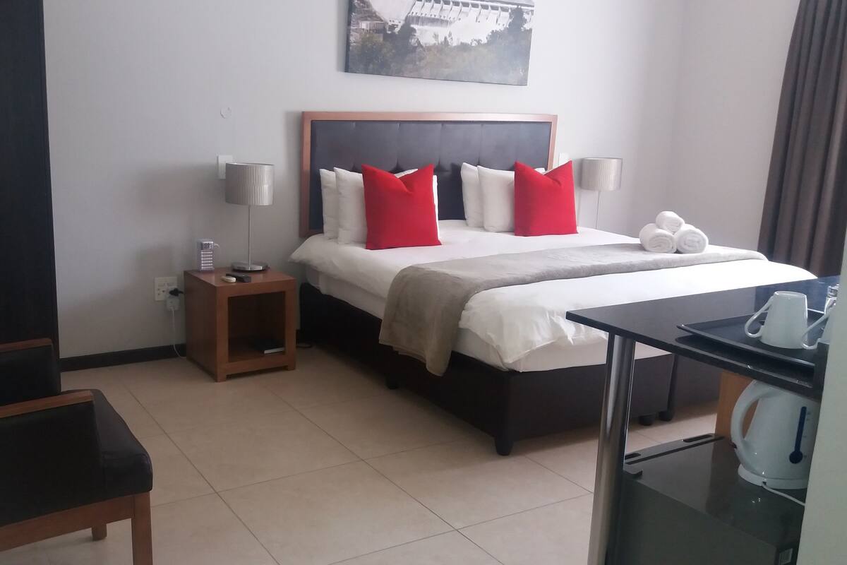 A hotel room with a bed, bedside tables, a desk, and a chair.