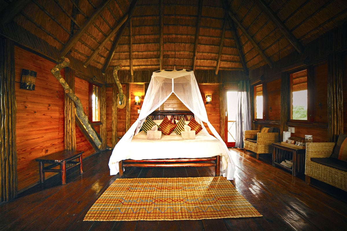 A wooden cabin room with a bed under a canopy, a small table, and a wicker sofa.