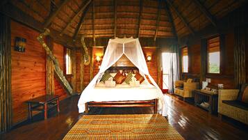 A wooden cabin room with a bed under a canopy, a small table, and a wicker sofa.