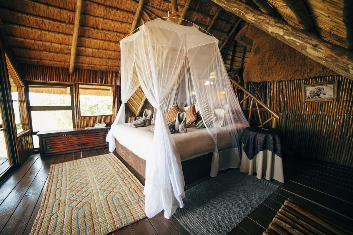 A room with a bed under a canopy, wooden floors, and a rustic thatched ceiling.